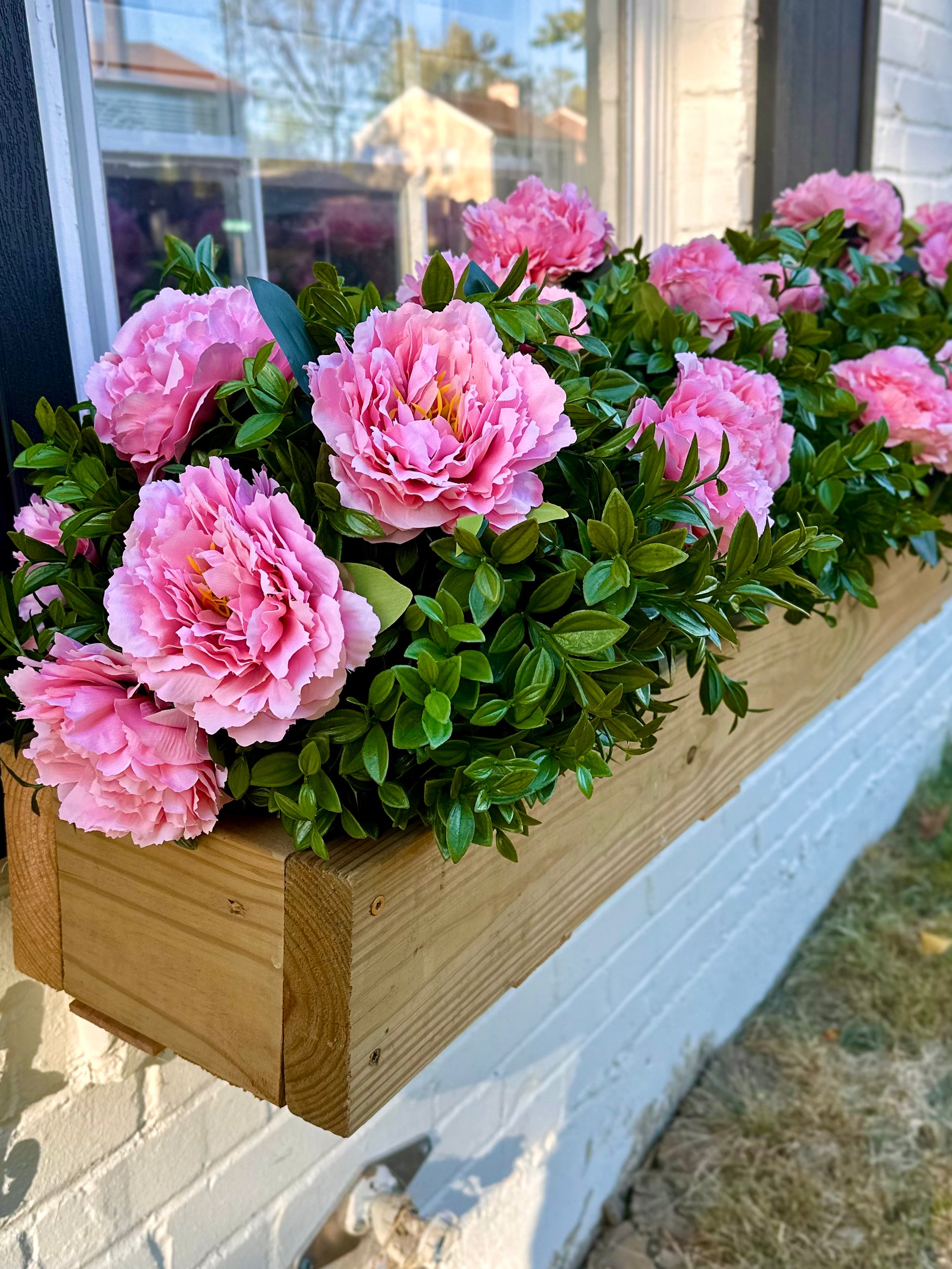 Realistic looking Fake Pink flowers in a wooden planter box on a windowsill.